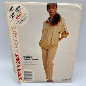 May include: A McCall's sewing pattern envelope for a two-piece outfit featuring a beige zip-up jacket with a collar and long sleeves, paired with matching straight-leg trousers. The envelope includes the text Stitch 'n Save, 4447, and Focus on Overlock.
