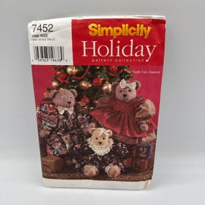 May include: A Simplicity Holiday pattern collection envelope, number 7452, featuring three teddy bears in festive outfits. The bears are positioned in front of a decorated Christmas tree. The text includes the brand name and pattern number.