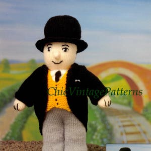 May include: Hand-knitted figure of a man in a black suit, yellow vest, and gray pants, wearing a black bowler hat. The figure has a smiling face and is standing on a surface with a background of a bridge and train tracks. The text "Chic Vintage Patterns" is visible.