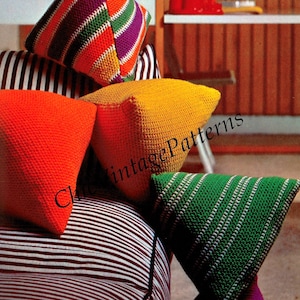 Puede incluir: Una colección de coloridos cojines de ganchillo de varias formas y tamaños. Los cojines presentan colores vibrantes como naranja, amarillo, verde y morado, con diseños a rayas y lisos. Los cojines están colocados sobre un cojín a rayas, creando un ambiente acogedor.