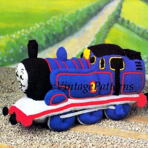 Peut inclure: Un train jouet bleu tricoté avec des détails rouges et jaunes. Le train a une cheminée noire et un visage souriant. Le numéro "1" est visible sur le côté. Le texte "Vintage Patterns" est imprimé sur le côté du train.