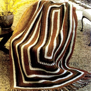 May include: A crocheted blanket with a geometric pattern in shades of brown, white, and olive green. The blanket has a fringed edge and is draped over a chair. The text "Vintage & Gift Patterns" is visible.