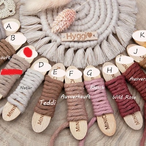 May include: A collection of cotton cord spools wrapped around wooden bobbins labeled with letters A through K. The cords come in various colors including pearl, brown, natural, teddy, blush, wild rose, and mustard yellow, with some marked as sold out.