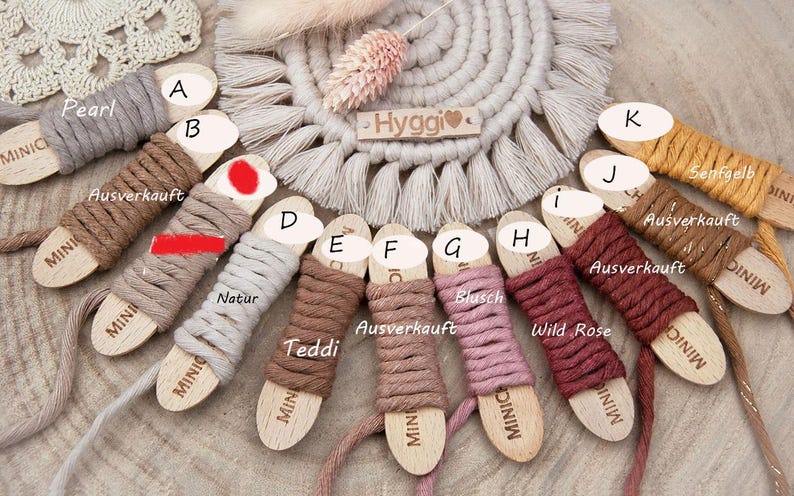 May include: A collection of cotton cord spools wrapped around wooden bobbins labeled with letters A through K. The cords come in various colors including pearl, brown, natural, teddy, blush, wild rose, and mustard yellow, with some marked as sold out.