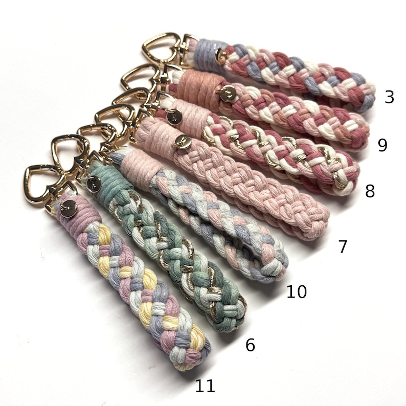 May include: A collection of six braided fabric keychains with gold-toned heart-shaped clasps and small circular metal tags. Each keychain features a unique color combination of pastel threads, some interwoven with metallic gold strands, labeled 3, 9, 8, 7, 10, 6, and 11.