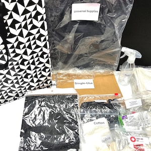 May include: A black and white geometric tote bag filled with various supplies, including a black face mask, a brown cardboard box labelled "Single-Use", a white spray bottle, a white washcloth, and a white cotton glove.