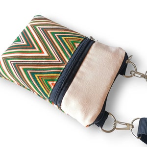 Puede incluir: Un pequeño bolso bandolera con cremallera, con un estampado de chevron colorido y un forro de lona beige. El bolso tiene una correa negra ajustable con cierres plateados.