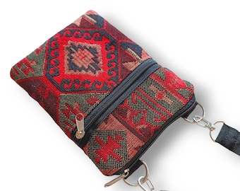 May include: A small rectangular crossbody bag featuring a woven fabric with a geometric pattern in shades of red, black, and dark green. The bag includes a black zippered closure, silver-toned metal hardware, and a black adjustable fabric strap.