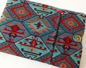 Pode incluir: Uma capa para laptop de tecido com padrão turquesa e vermelho com fecho de botão.