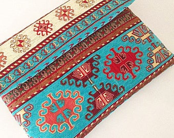 Pode incluir: Uma carteira de mão de tecido turquesa, vermelho e creme com um padrão geométrico. A carteira de mão está dobrada ao meio e o padrão é visível em ambos os lados.