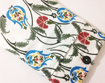 Pode incluir: Uma bolsa de tecido branco com um padrão floral em tons de azul, vermelho, verde e amarelo. A bolsa tem um fecho de botão.