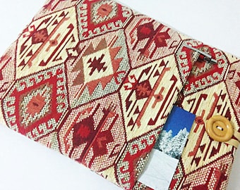 Pode incluir: Uma capa para laptop de tecido estampado em vermelho, bege e marrom, com um bolso e um fecho de botão de madeira.