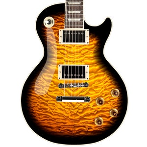 Puede incluir: Una guitarra eléctrica dorada y negra con una tapa de arce flameado. La guitarra tiene una golpeador negro y herrajes dorados.
