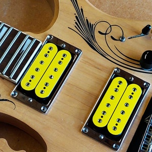 May include: A close-up of a wooden electric guitar with two yellow humbucker pickups. The guitar has a black and white swirl design on the body.