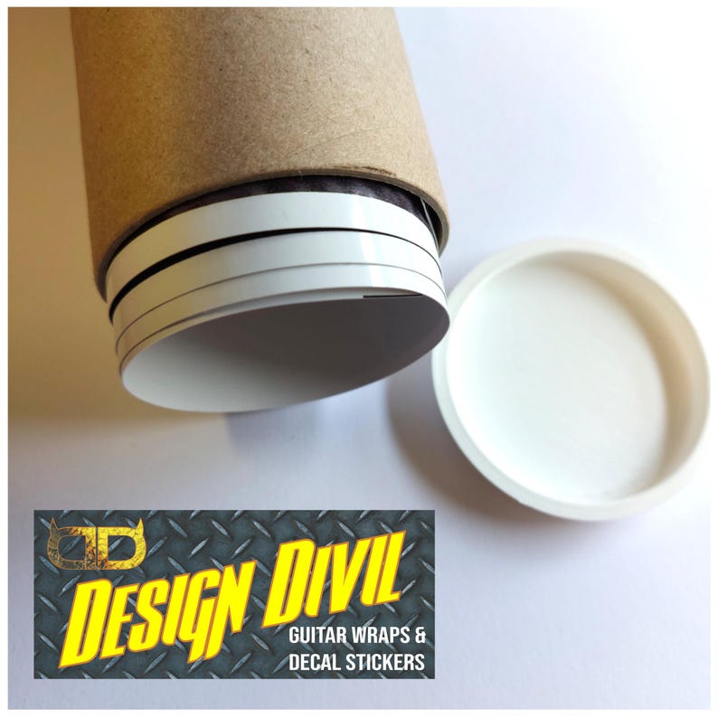 May include: A cylindrical brown cardboard mailing tube with a white plastic cap, containing rolled white decal stickers. A rectangular logo graphic features the text DESIGN DIVIL GUITAR WRAPS & DECAL STICKERS in yellow on a gray diamond plate pattern.