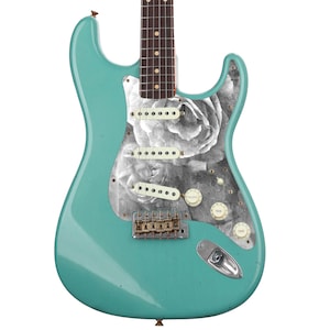 May include: A teal electric guitar with a black and white rose graphic on the body. The guitar has a rosewood fretboard and chrome hardware.