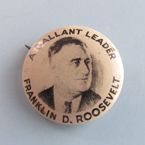 May include: Vintage button featuring a portrait of Franklin D. Roosevelt with the text "A Gallant Leader" and "Franklin D. Roosevelt" in a circular design. The button is a light tan color with black text and a pin on the back.