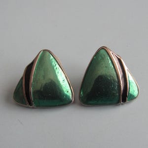 May include: A pair of triangular earrings with a metallic green finish. The earrings have a bronze-colored border and a black stripe detail. The earrings are displayed on a white surface.