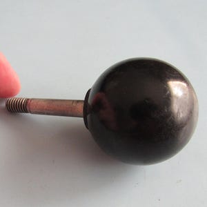 May include: A spherical black knob attached to a silver-colored metal threaded bolt. The knob has a smooth, glossy finish and a rounded shape, while the metal bolt features visible screw threads extending from the base of the sphere.