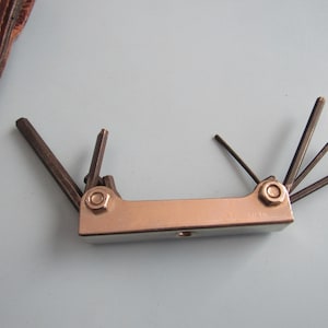 May include: A multi-tool hex key set with a silver metal body and several black hex keys of varying sizes. The tool is designed for tightening or loosening screws with hexagonal sockets. The tool is shown against a light blue background.