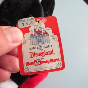 May include: A black plush toy with a red tag. The tag reads "MADE EXCLUSIVELY FOR Disneyland and Walt Disney World." The tag also shows a castle graphic and the price $6.00. The toy has black ears and a red and yellow design.