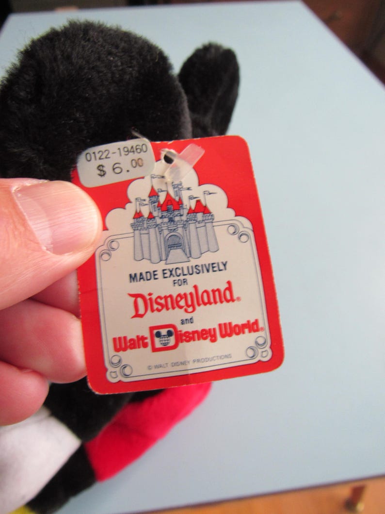 May include: A black plush toy with a red tag. The tag reads "MADE EXCLUSIVELY FOR Disneyland and Walt Disney World." The tag also shows a castle graphic and the price $6.00. The toy has black ears and a red and yellow design.