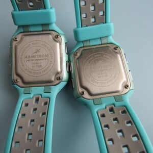 May include: Two Armitron Pro Sport digital watches with teal and gray straps. The stainless steel backs display the brand name, model number, and water resistance details. The watches have an acrylic case and are water resistant to 165 feet.