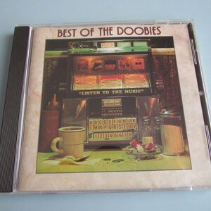 May include: CD case for "Best of The Doobies" album. The cover art features a diner scene with a jukebox, coffee cup, and condiments. The text "LISTEN TO THE MUSIC" is visible on the jukebox. The CD case is in a clear plastic case.