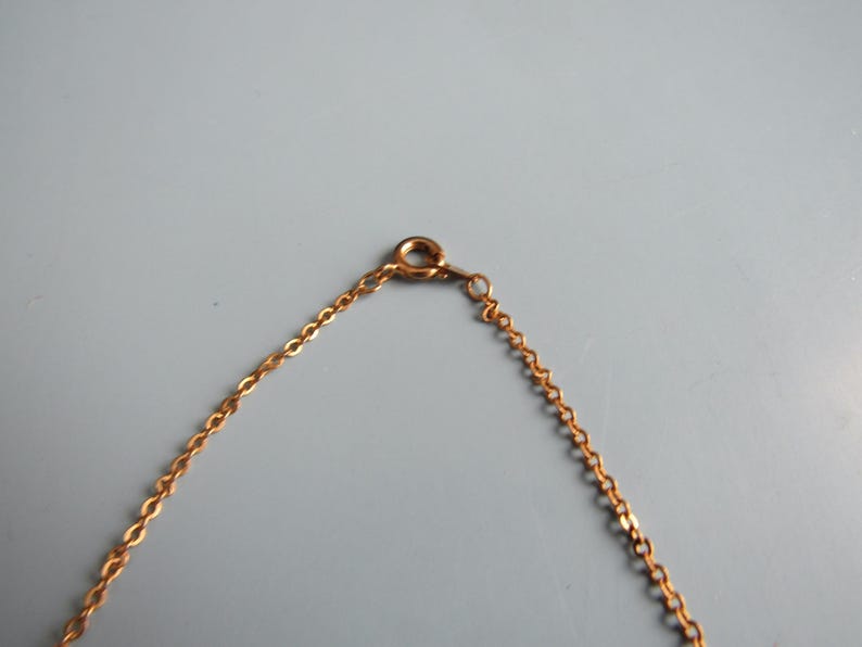 May include: A gold-colored necklace chain with a lobster clasp. The chain is made of small, interconnected links. The clasp is attached to a small ring. The background is a solid, light gray color.