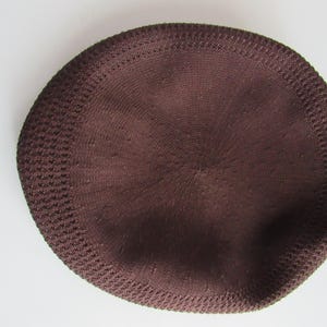 May include: A dark brown knitted skullcap with a rounded crown and a textured edge. The cap is a solid colour and appears to be made of a soft, breathable material. The cap is circular in shape.