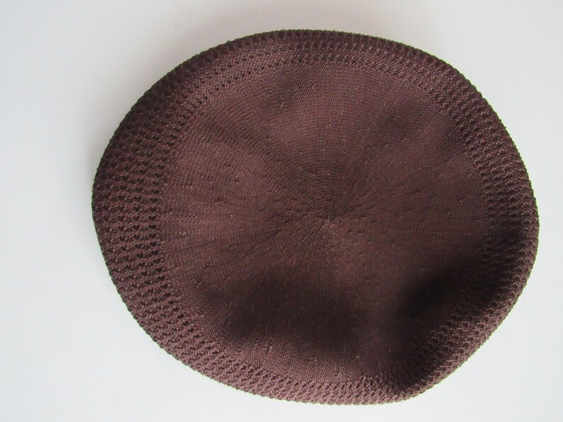 May include: A dark brown knitted skullcap with a rounded crown and a textured edge. The cap is a solid colour and appears to be made of a soft, breathable material. The cap is circular in shape.