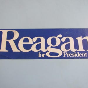 May include: A blue rectangular sticker with the white text "Reagan for President". The word "Reagan" is in a large, bold font, and "for President" is in a smaller font below.