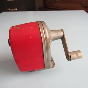 May include: A vintage red and silver pencil sharpener with a crank handle.