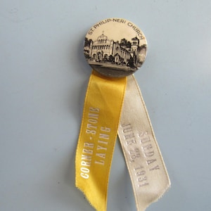 May include: A yellow and white ribbon with the text "ST. PHILIP-NERI CHURCH", "CORNER-STONE LAYING", and "SUNDAY JUNE 28, 1931" printed on it. A small button with a black and white image of a church is attached to the ribbon.