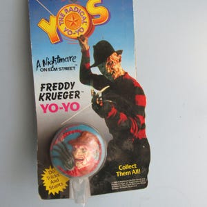 May include: A Nightmare on Elm Street Freddy Krueger yo-yo toy. The yo-yo is blue and features a red and white image of Freddy Krueger's face. The packaging is red, white, and blue with the text "The Radical Yo-Yos" and "Collect Them All!"