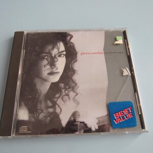 May include: A compact disc case with a photo of Gloria Estefan on the front. The case is black and silver with a white sticker that says "Best Value". The title of the album is "Cuts Both Ways".