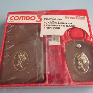 May include: A vintage Combo 3 gift set by Fran Stef, featuring a Scripto lighter, cigarette case, and key fob. The brown leather-like items have a gold rose emblem. The set is packaged in a red box.