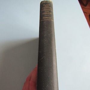 May include: A dark green hardcover book spine with gold lettering. The text reads PLANE AND SPHERICAL TRIGONOMETRY AND TABLES, DURELL, and MERRILL. The book has a textured fabric cover and shows signs of wear along the edges and corners.