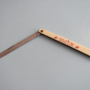 May include: An open, vintage pocket knife with a cream-colored handle and a silver blade. The handle features red text and graphics that read "SWIFT'S PREMIUM TABLE READY MEATS."
