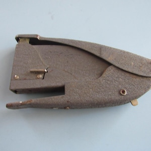 May include: A vintage, gray stapler with a textured surface. The stapler has a curved handle and a lever on the side. It is made of metal and has a classic design.