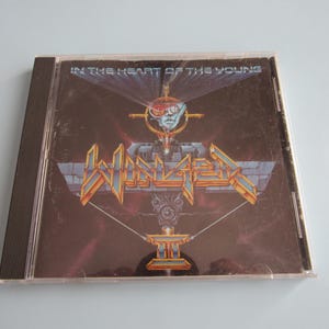 May include: A compact disc case with a black and silver design. The album cover features the band "Winger" and the album title "In the Heart of the Young".