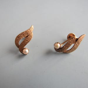 May include: A pair of gold tone clip-on earrings with a textured leaf design and a single pearl accent on each earring.