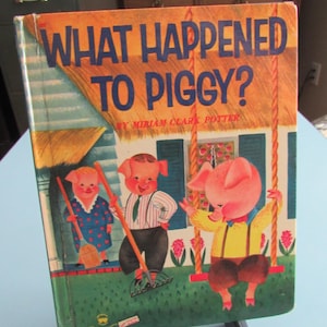 May include: Vintage children's book titled "What Happened to Piggy?" with illustrations of three pigs. The cover features a house and a pig on a swing. The book is propped up on a black stand.