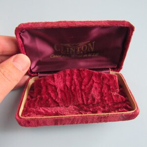 May include: A red velvet watch box with gold lettering that reads "Clinton Watches, Case and movement made in U.S.A."
