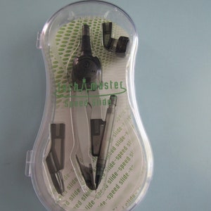 May include: A black compass with a clear plastic case. The compass has a silver metal body and a black plastic handle. The case has a green and white pattern with the words "Speed Slide" printed on it.