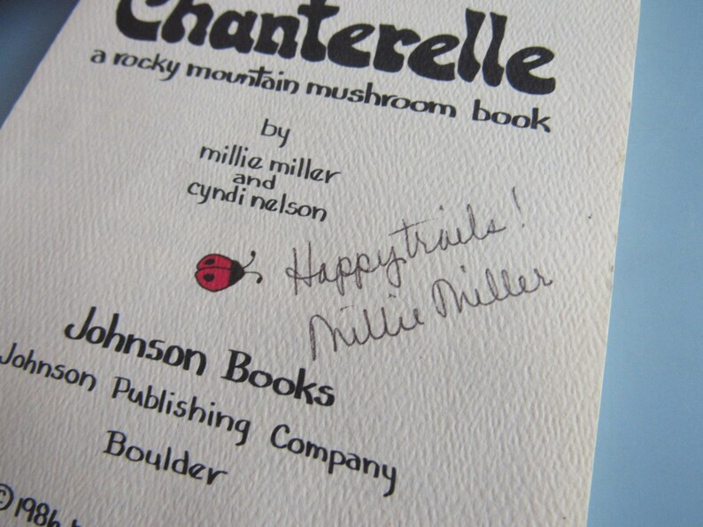 May include: Close-up of a book cover titled "Chanterelle," a rocky mountain mushroom book. The cover features text, including the authors' names, and a handwritten note with a ladybug illustration. Published by Johnson Books.