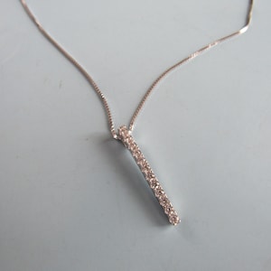 May include: A silver chain necklace with a pendant that is a thin bar of metal with small clear stones set into it.