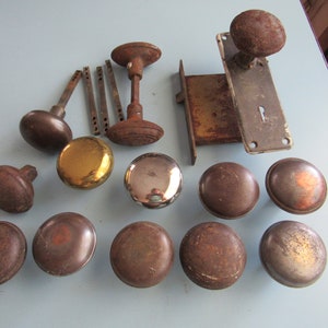 May include: A collection of vintage door knobs and a door lock plate. The knobs are made of metal and have a variety of finishes, including brass, chrome, and nickel. The door lock plate is made of metal and has a keyhole.