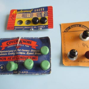 May include: Three vintage cardboard display cards holding replacement knobs. One red and blue card features two black knobs. A blue card holds four light green knobs labeled non-heat conducting. An orange card displays three knobs in black and maroon.