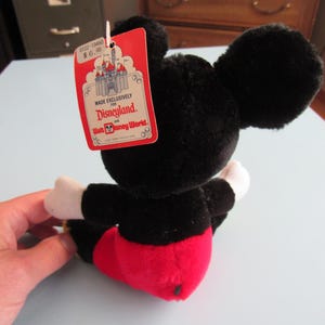 May include: A black plush Mickey Mouse toy with red shorts, white gloves, and large black ears. The toy has a red tag that reads "Made Exclusively For Disneyland and Walt Disney World."